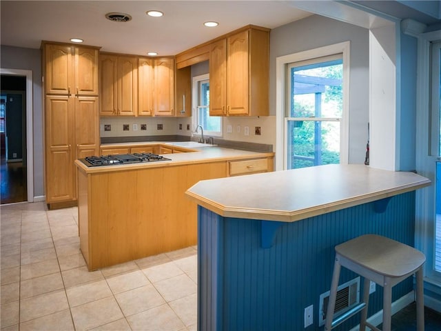 kitchen with light tile patterned floors, a kitchen island, light countertops, stainless steel gas stovetop, and a sink