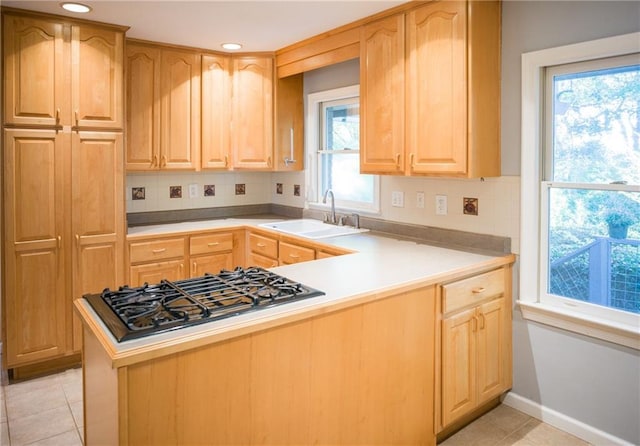 kitchen featuring light tile patterned flooring, a peninsula, a sink, light countertops, and stainless steel gas stovetop