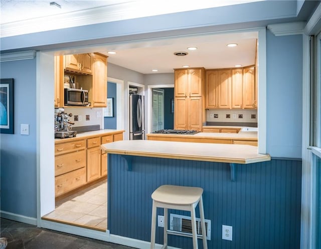 kitchen with visible vents, appliances with stainless steel finishes, a breakfast bar area, light countertops, and light brown cabinets