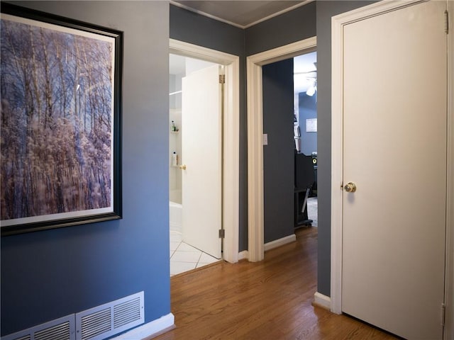 hall featuring baseboards, visible vents, and wood finished floors