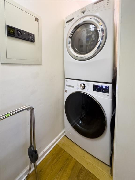 laundry area with stacked washing maching and dryer, laundry area, baseboards, and wood finished floors