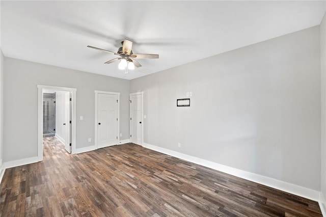 unfurnished bedroom with baseboards, dark wood-type flooring, ensuite bathroom, and ceiling fan