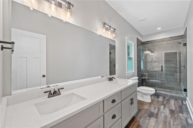 bathroom featuring toilet, a stall shower, double vanity, and wood finished floors