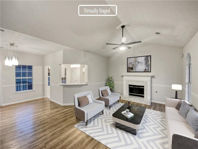 living room with ceiling fan with notable chandelier, a fireplace, lofted ceiling, and hardwood / wood-style floors