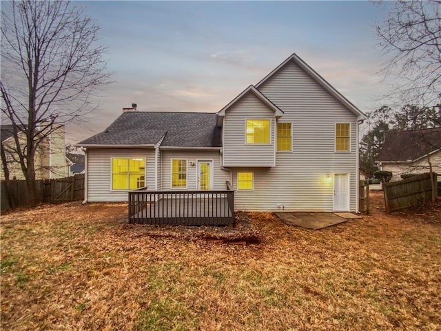 back house at dusk with a patio, a wooden deck, and a lawn