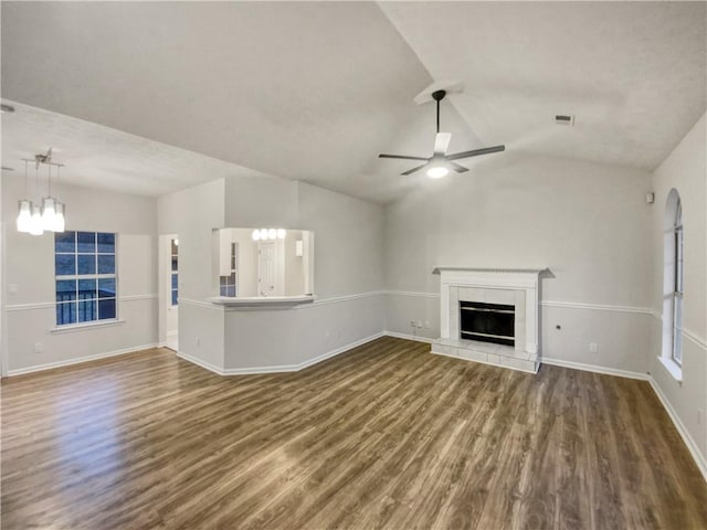 unfurnished living room with dark wood-type flooring, a tile fireplace, lofted ceiling, and ceiling fan with notable chandelier