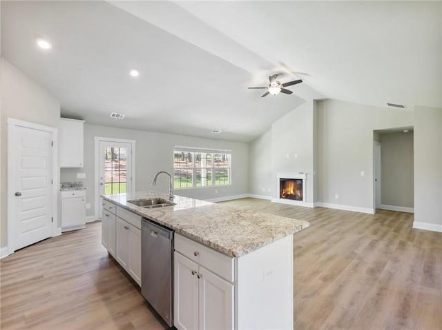 kitchen with stainless steel dishwasher, a glass covered fireplace, white cabinets, vaulted ceiling, and a sink