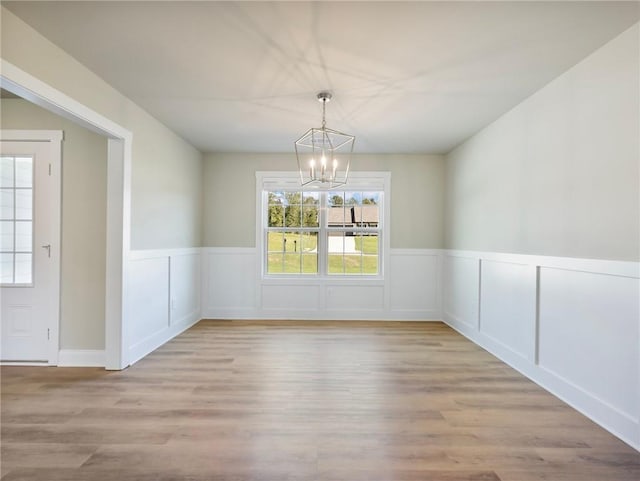 unfurnished dining area featuring wood finished floors, a wainscoted wall, and an inviting chandelier