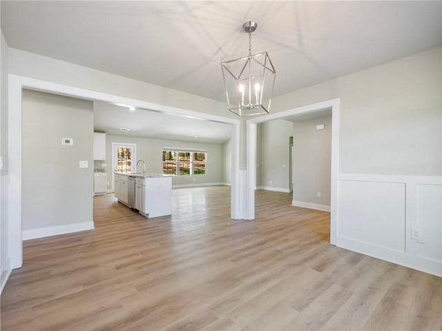 unfurnished living room with baseboards, a notable chandelier, a sink, and light wood finished floors