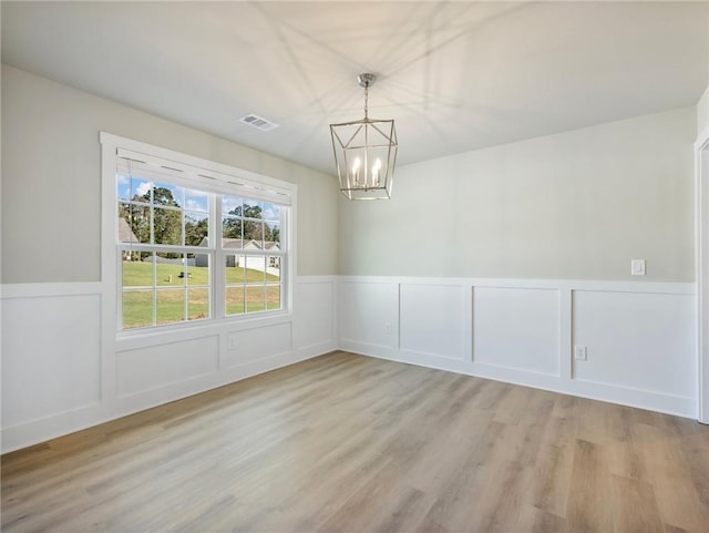 unfurnished dining area featuring light wood-style floors, a wainscoted wall, visible vents, and an inviting chandelier