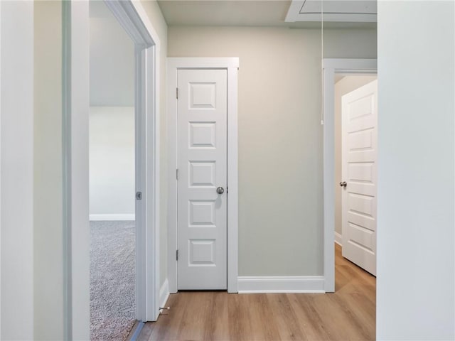 hallway featuring light wood-style floors, attic access, and baseboards