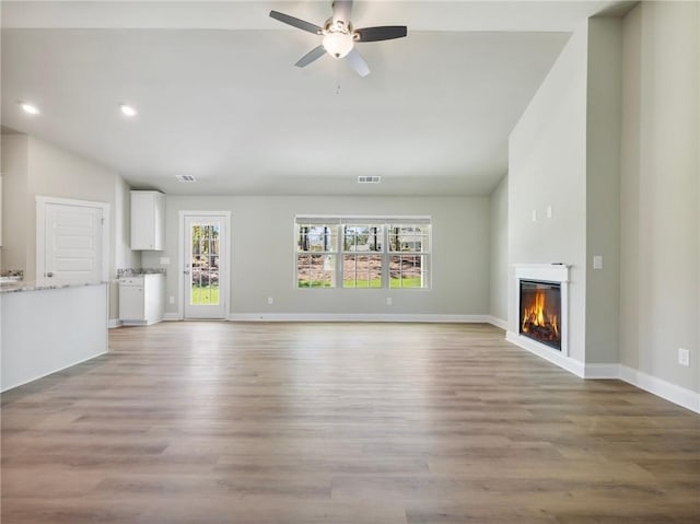 unfurnished living room featuring ceiling fan, lofted ceiling, light wood-style flooring, baseboards, and a glass covered fireplace