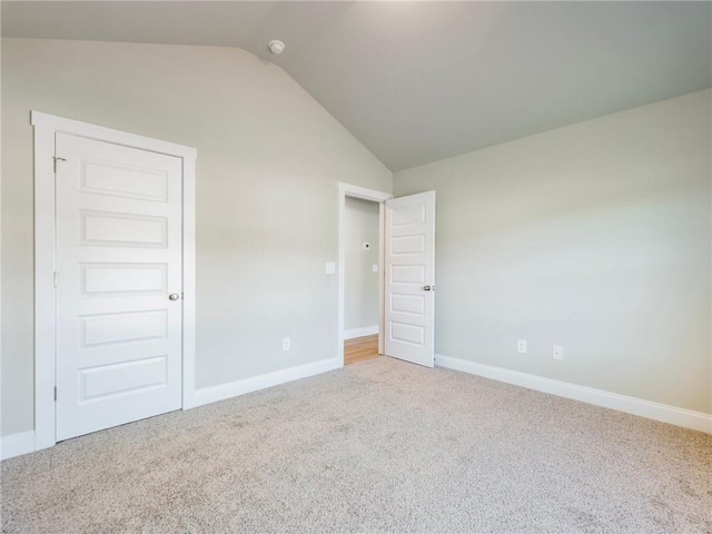 carpeted empty room with vaulted ceiling and baseboards