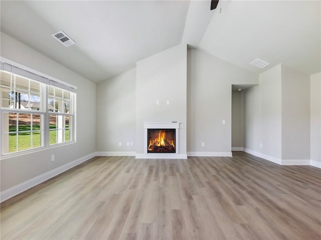 unfurnished living room featuring visible vents, baseboards, lofted ceiling, light wood-style flooring, and a lit fireplace