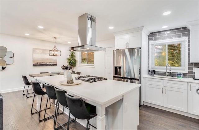 kitchen with a kitchen bar, white cabinetry, hanging light fixtures, island exhaust hood, and stainless steel appliances