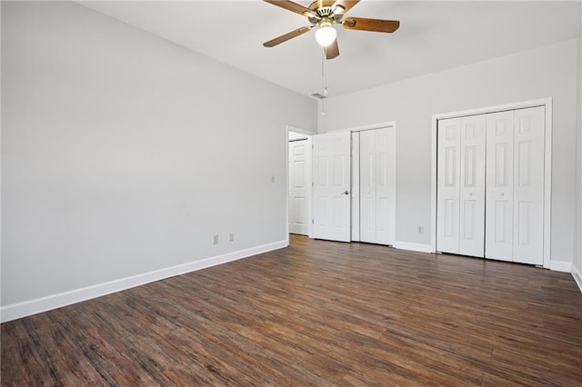 unfurnished bedroom featuring baseboards, multiple closets, dark wood-type flooring, and ceiling fan