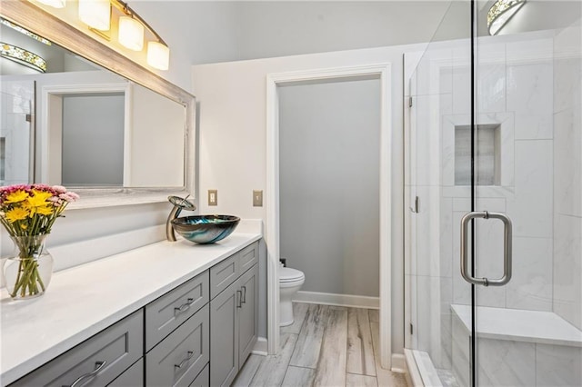 bathroom featuring vanity, wood finished floors, baseboards, a shower stall, and toilet