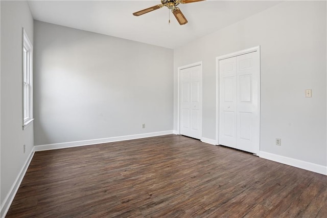 unfurnished bedroom with baseboards, multiple closets, ceiling fan, and dark wood-style flooring