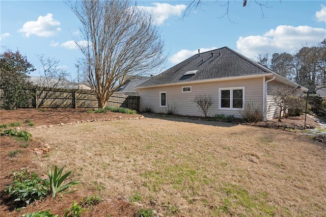 view of side of property featuring fence, a lawn, and a shingled roof