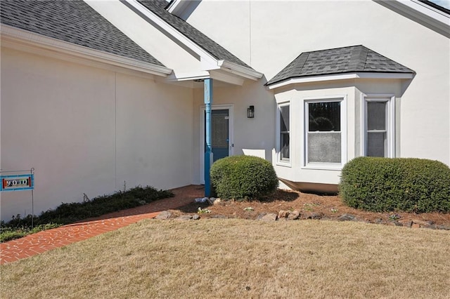 entrance to property with a yard, roof with shingles, and stucco siding