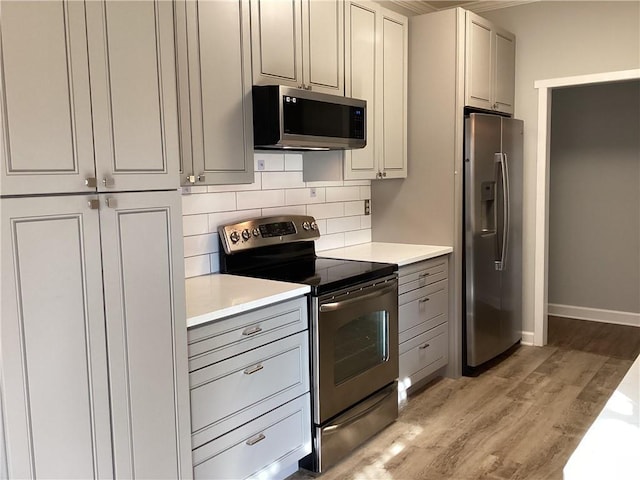 kitchen with decorative backsplash, light countertops, light wood finished floors, and appliances with stainless steel finishes