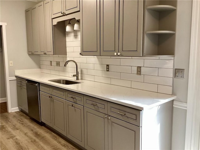 kitchen featuring gray cabinets, a sink, light wood-style floors, decorative backsplash, and dishwasher