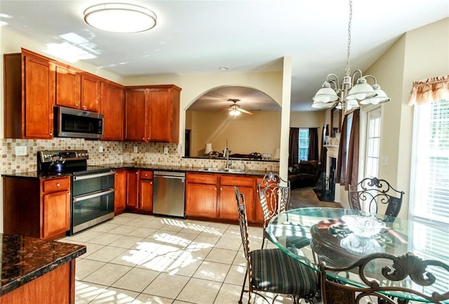 kitchen with appliances with stainless steel finishes, dark stone counters, sink, backsplash, and light tile patterned flooring