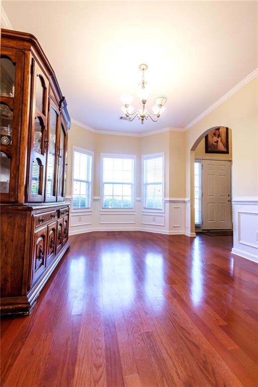 unfurnished living room featuring dark hardwood / wood-style floors, ornamental molding, and an inviting chandelier