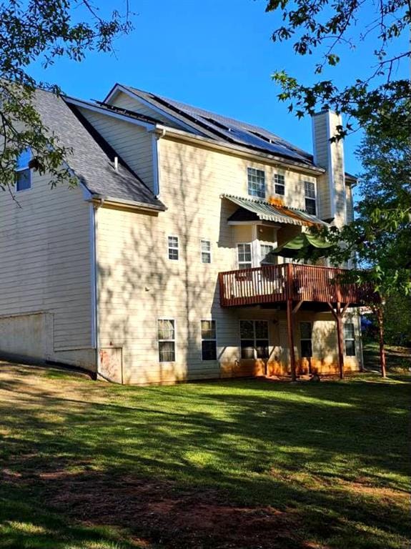 rear view of house with solar panels, a wooden deck, and a yard