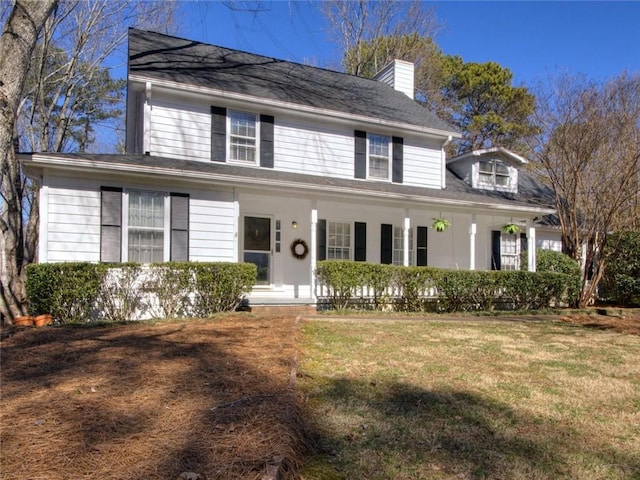 view of front facade with covered porch, a chimney, and a front lawn