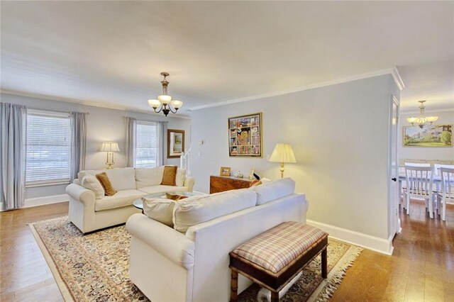 living room featuring ornamental molding, light wood-type flooring, a notable chandelier, and baseboards