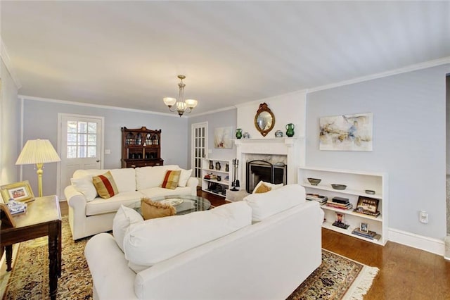 living area featuring baseboards, ornamental molding, dark wood-style flooring, a chandelier, and a high end fireplace