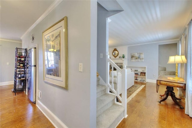 hallway featuring stairs, light wood-style floors, baseboards, and crown molding