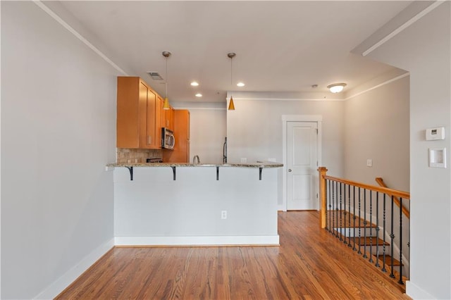 kitchen featuring kitchen peninsula, wood-type flooring, decorative light fixtures, and a breakfast bar area