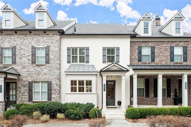 townhome / multi-family property with a standing seam roof, brick siding, metal roof, and roof with shingles