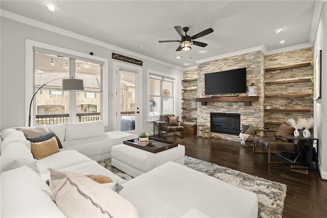 living area with ornamental molding, a ceiling fan, a stone fireplace, and wood finished floors