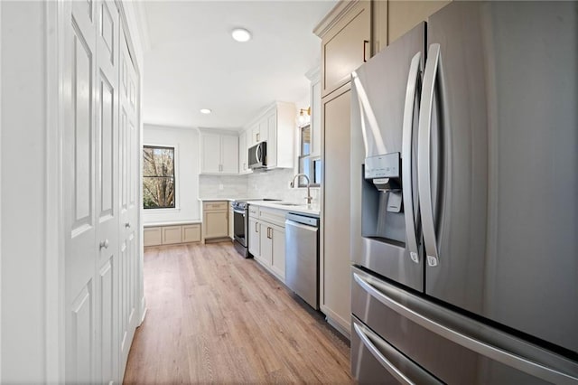 kitchen featuring a sink, light wood-style floors, light countertops, appliances with stainless steel finishes, and decorative backsplash