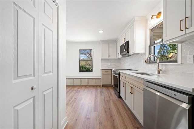 kitchen with tasteful backsplash, appliances with stainless steel finishes, light countertops, light wood-style floors, and a sink