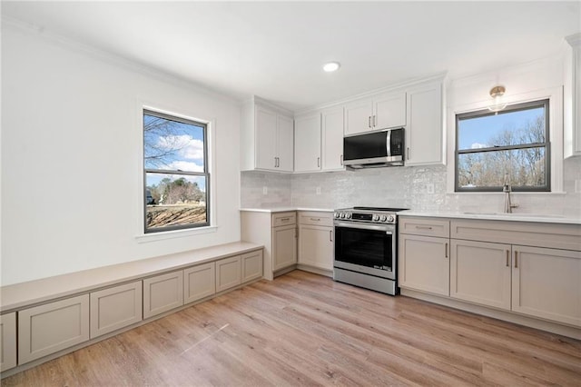 kitchen featuring stainless steel appliances, a sink, light wood-style floors, tasteful backsplash, and plenty of natural light