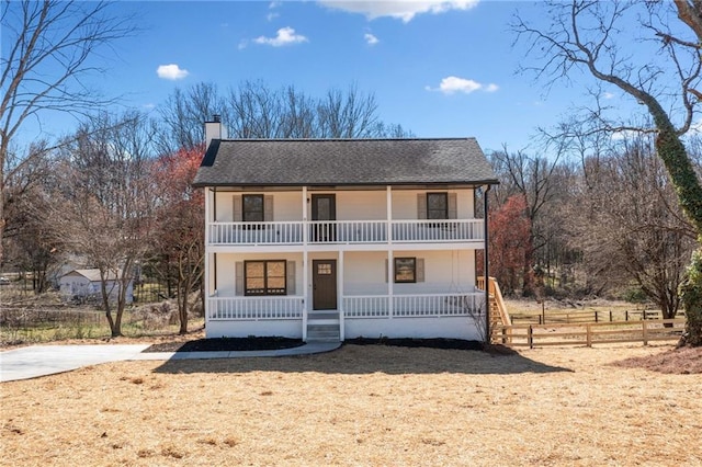 view of front of home with a shingled roof, a balcony, a chimney, fence, and a porch