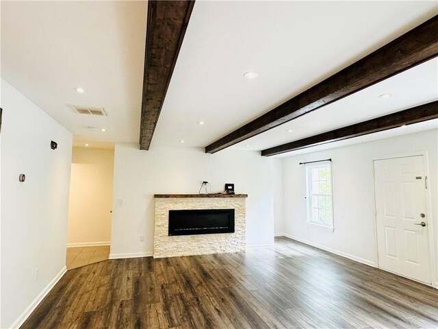 unfurnished living room with wood-type flooring, a stone fireplace, and beam ceiling