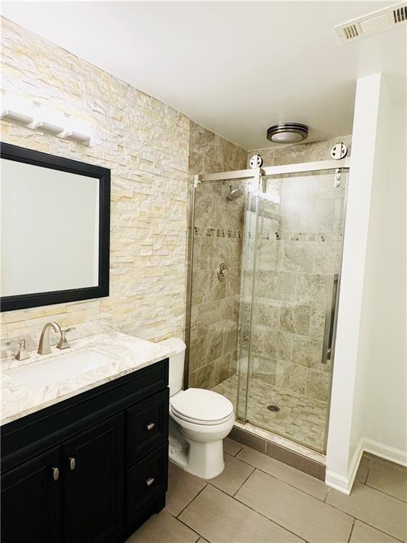 bathroom with tile patterned floors, vanity, toilet, and a shower with shower door