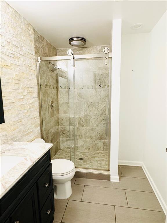 bathroom with tile patterned flooring, vanity, an enclosed shower, and toilet