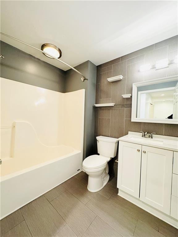 full bathroom featuring shower / bathing tub combination, vanity, tile walls, and toilet