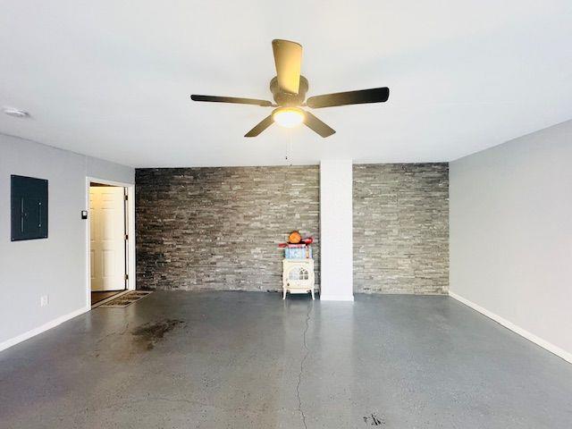 interior space featuring electric panel, ceiling fan, and brick wall