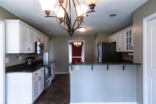 kitchen with kitchen peninsula, white cabinets, appliances with stainless steel finishes, and an inviting chandelier