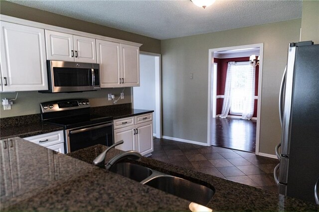 kitchen with dark stone countertops, white cabinets, a textured ceiling, and stainless steel appliances