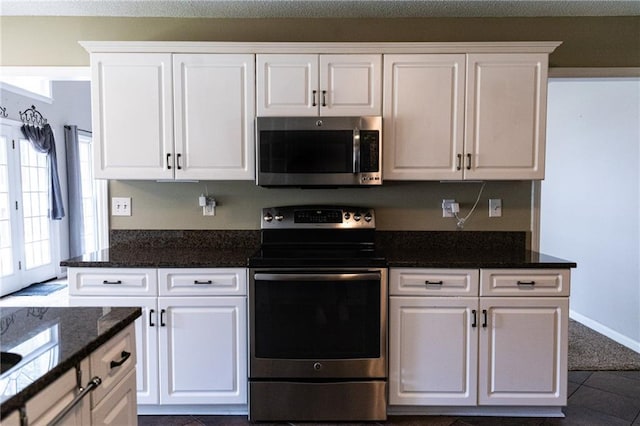 kitchen with stainless steel appliances, dark tile patterned floors, and white cabinetry