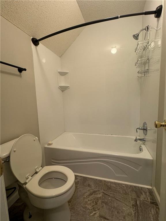 bathroom featuring washtub / shower combination, vaulted ceiling, a textured ceiling, and toilet