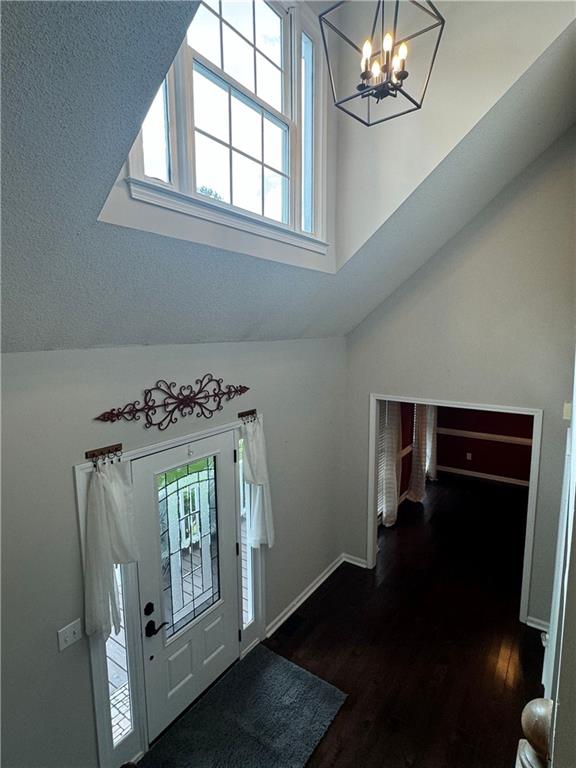 foyer entrance featuring a wealth of natural light, dark wood-type flooring, vaulted ceiling, and an inviting chandelier